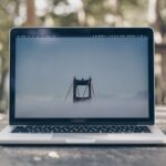 A laptop displaying a foggy bridge on its screen, placed on a wooden table in a natural setting.