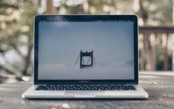A laptop displaying a foggy bridge on its screen, placed on a wooden table in a natural setting.